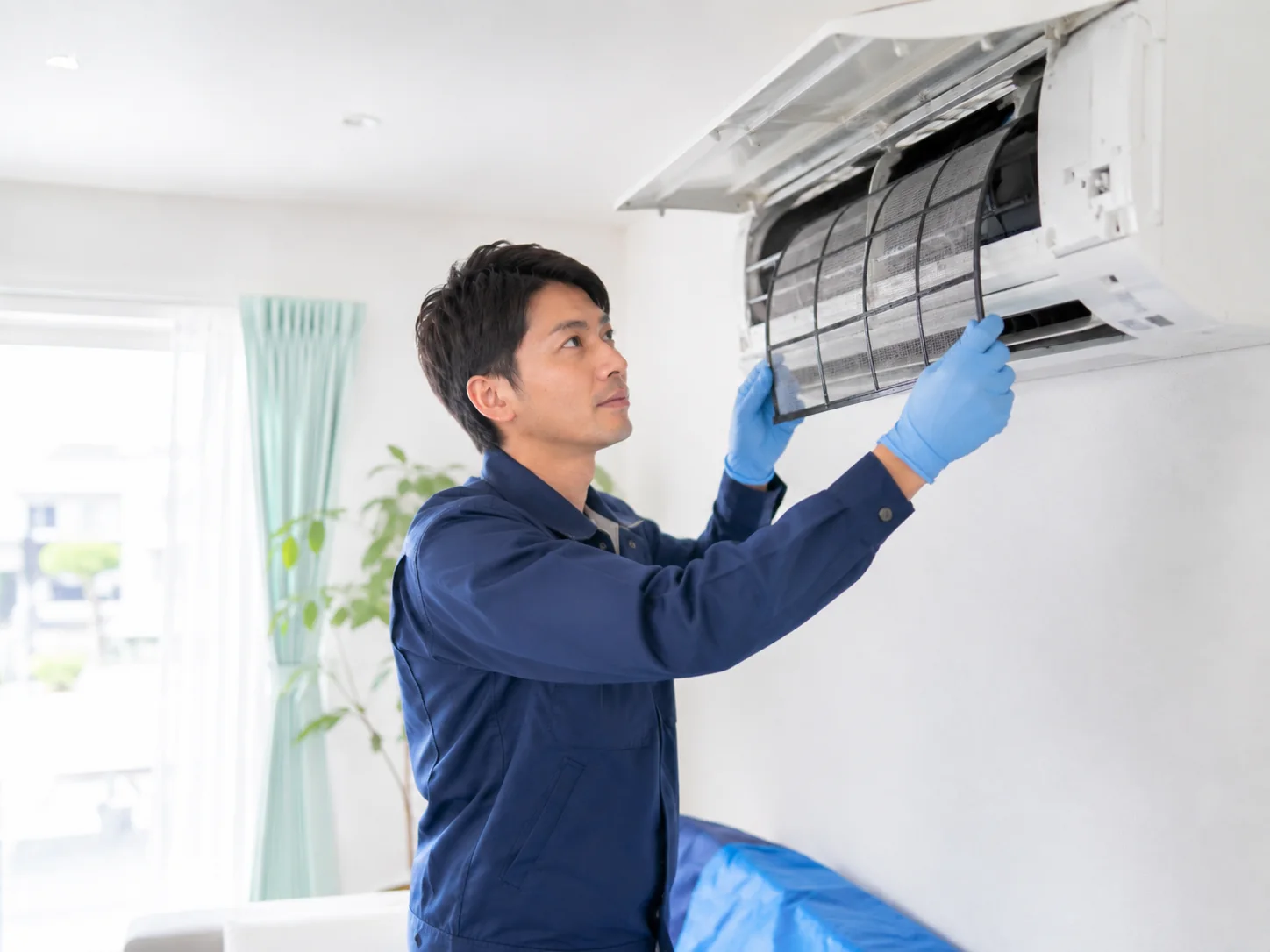 住宅の壁掛けエアコンを点検する訪問スタッフ